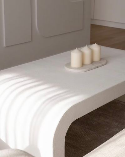 Close-up of a curved white ribbed coffee table with three candles on a marble tray