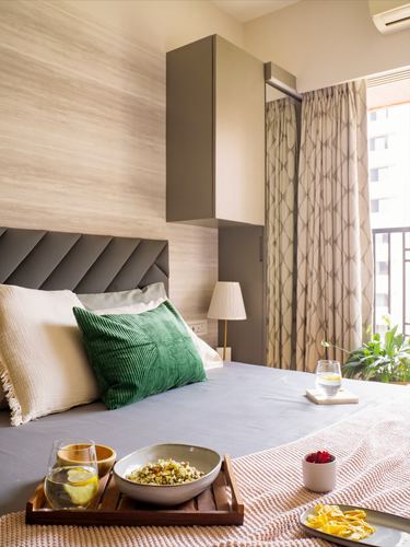 Bedroom with chevron grey headboard, green cushion, breakfast tray on bed, balcony curtains open