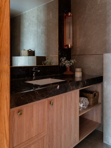 Bathroom vanity with dark marble counter, wood cabinetry, and brass wall sconce