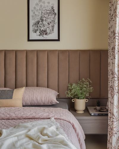 Bedroom with brown channel-tufted headboard, pink bedding, and floral curtain beside nightstand with vase