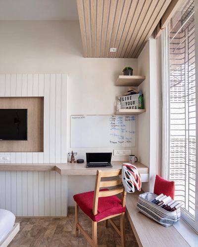 Study nook with wood desk, whiteboard, laptop, red chair, and slatted ceiling by window