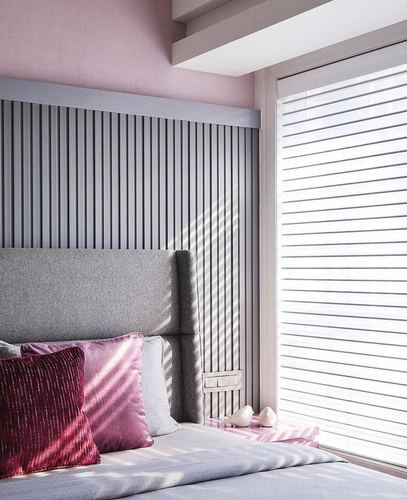 Grey fluted headboard wall in pink bedroom with sunlight through sheer blinds and velvet cushions