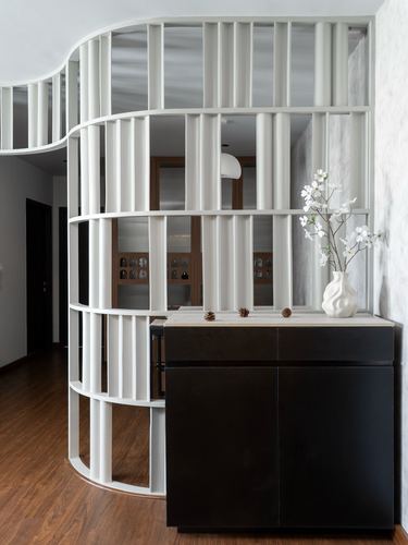 Curved white slatted screen beside a dark console with a white vase in a foyer