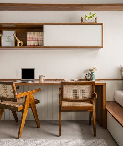Wooden study desk with cane armchairs beneath a floating wall shelf with sliding white panel
