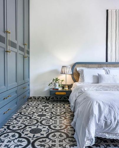 Pastel blue bedroom with cane headboard, patterned black and white floor tiles, and wardrobe with brass handles