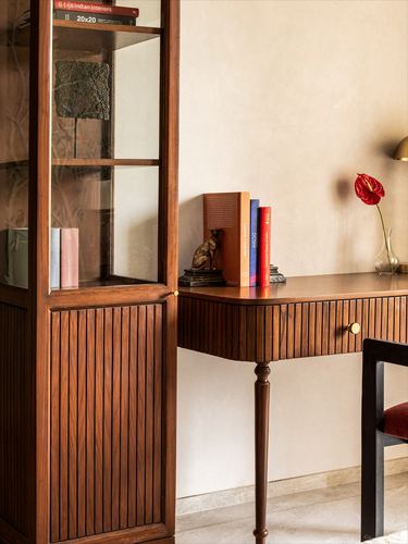 Fluted wood cabinet beside a ribbed desk with books, a bronze cat figurine, and a red anthurium