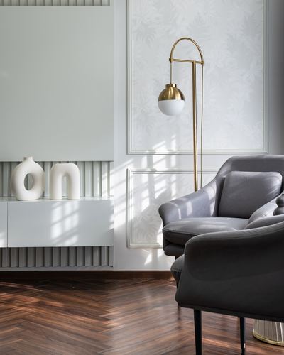 Grey velvet armchairs beside a brass arc lamp against white fluted panelling and herringbone floor