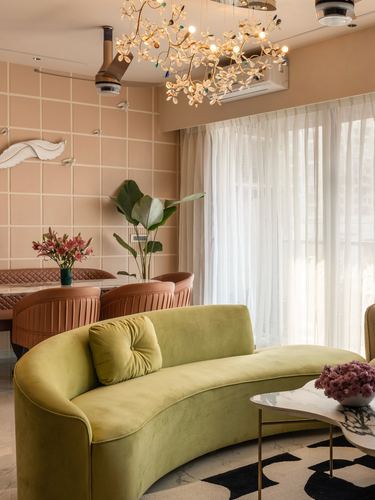 Curved chartreuse velvet sofa in front of peach tiled wall with floral chandelier and dining area beyond