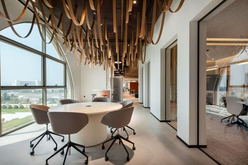 Office meeting nook with round table beneath a sculptural wood-loop ceiling and arched window overlooking the city