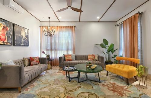 Living room with grey tufted sofas, marble coffee tables, mustard bench and floral rug