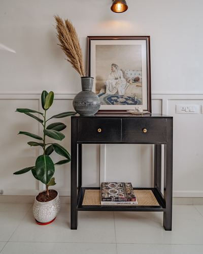 Black console table with framed art, vase, pampas grass, and plant against paneled wall