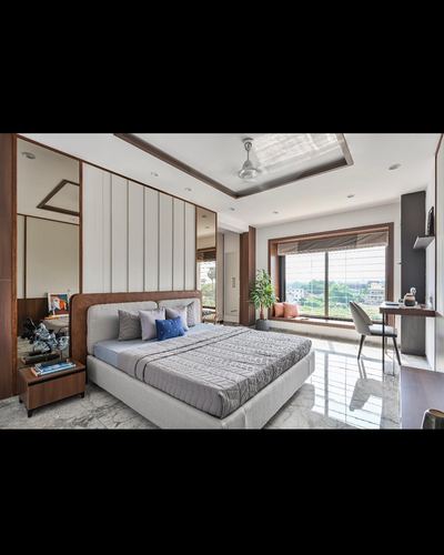 Contemporary bedroom with upholstered bed, fluted wood headboard wall, mirrors, and window seat with city view