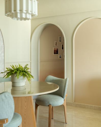 Dining nook with round stone table, sage chairs, and arched doorway to a framed gallery wall
