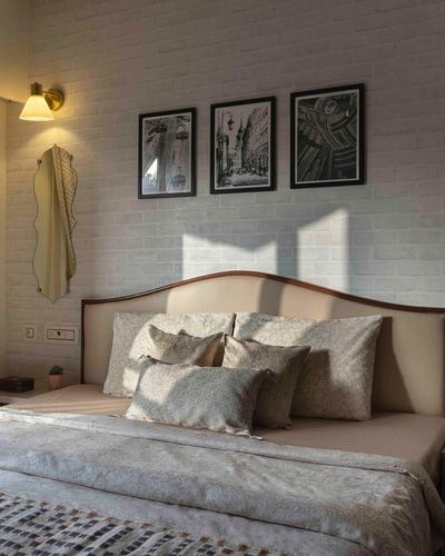 Bedroom with whitewashed brick wall, curved wood-trimmed headboard, patterned pillows, and three framed prints