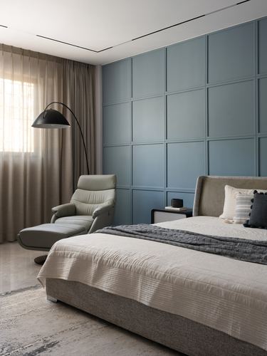 Bedroom with blue paneled accent wall, upholstered bed, and green leather recliner by curtained window