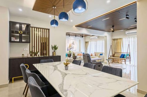 Open plan dining area with marble table, navy velvet chairs, and blue pendant lights leading to living room