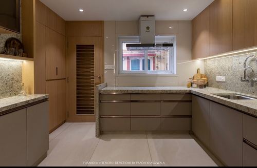 U-shaped kitchen with beige cabinetry, granite counters, wooden tall units and a chimney hood over the stove.