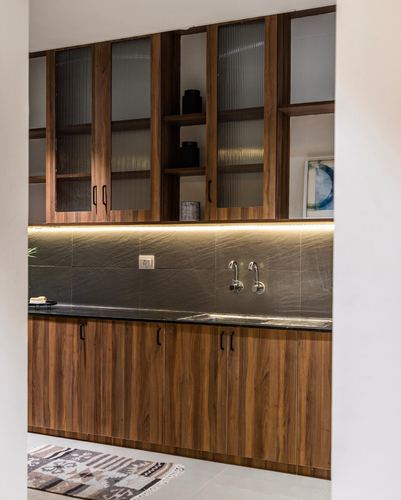 Kitchen view through doorway with wood cabinetry, fluted glass uppers, and wall-mounted faucet over dark stone counter