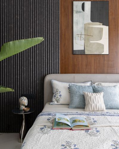 Bedroom with fluted dark panel wall, wood backdrop, abstract art, and blue-patterned bedding