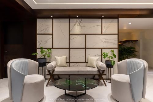 Living room with two curved velvet armchairs, a bench, and a marbled brass-gridded wall panel