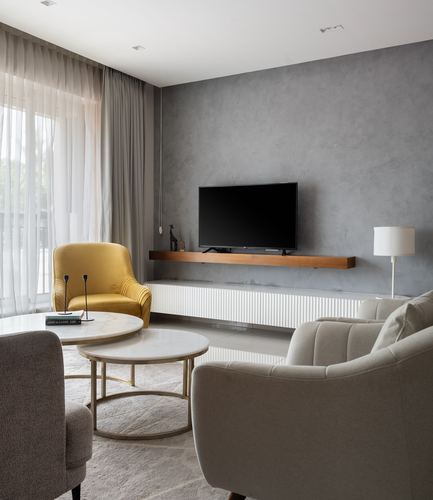 Grey textured living room wall with mounted TV, floating wood console, mustard chair and round marble coffee tables