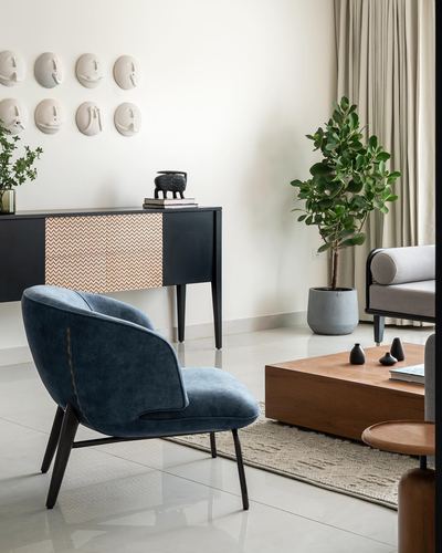 Living room with blue velvet chair, black console with patterned front, and wall of ceramic masks