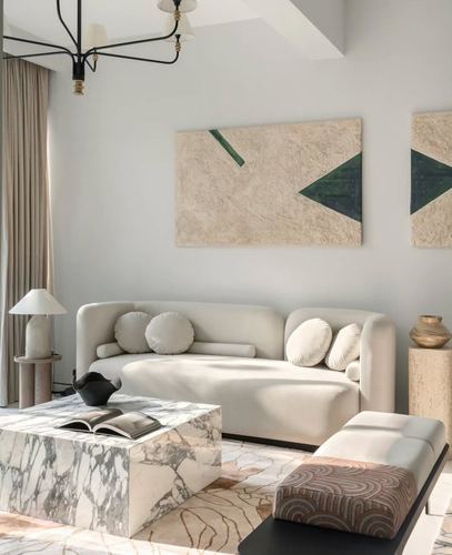 Cream curved sofa beside a veined marble coffee table under textured green-accented wall art