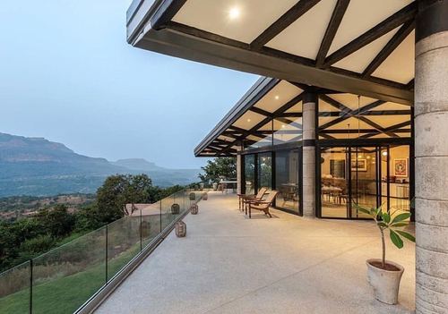 Covered terrace with exposed steel trusses overlooking hazy mountain valley at dusk