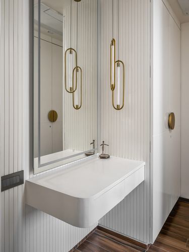 Floating white vanity with mirror and brass pendant lights against fluted paneled wall