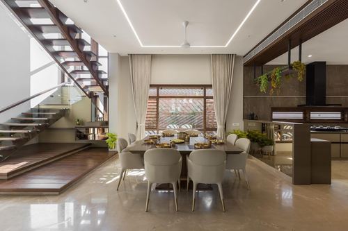 Open-plan dining area with wood staircase, upholstered chairs and glimpse into kitchen