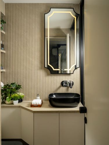 Corner bathroom vanity with black vessel sink, backlit mirror, and ribbed beige wall panelling
