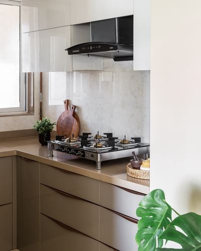 L-shaped kitchen corner with black gas hob, chimney hood, marble-look backsplash, and glossy beige cabinetry