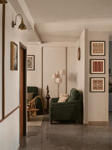 Hallway with framed prints leading to a living room with a green armchair and floor lamp