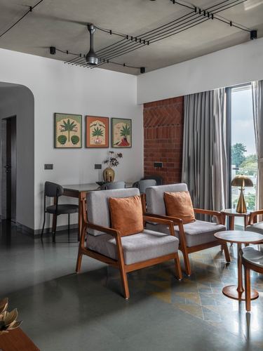 Living and dining area with wooden armchairs, patterned floor tile, and an exposed brick wall by a window