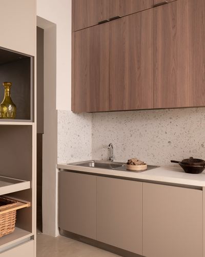 Modern kitchen corner with wood-veneer uppers, terrazzo backsplash, and taupe base cabinets