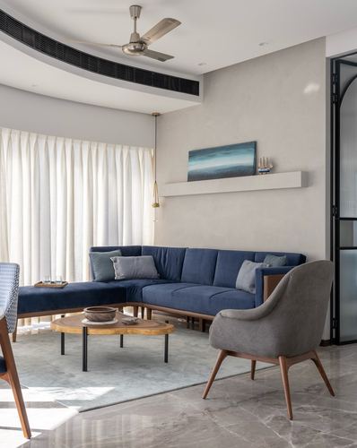 Living room with navy blue L-shaped sofa, wooden coffee table, and floating wall shelf with art