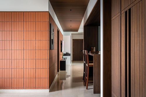 Corridor with terracotta tile wall leading to wood-paneled dining area in Chennai apartment