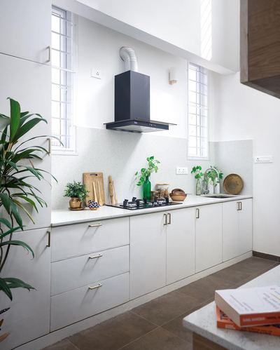 White modular kitchen with black chimney hood, terrazzo backsplash, brass accents and potted plants