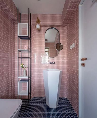 Pink mosaic tiled bathroom with sculptural white sink, oval mirror, and navy tile floor