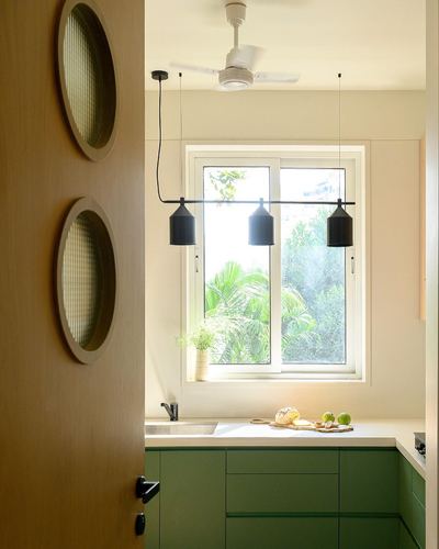 Kitchen seen through a wooden door with oval glass cutouts, green cabinetry and black pendant lights