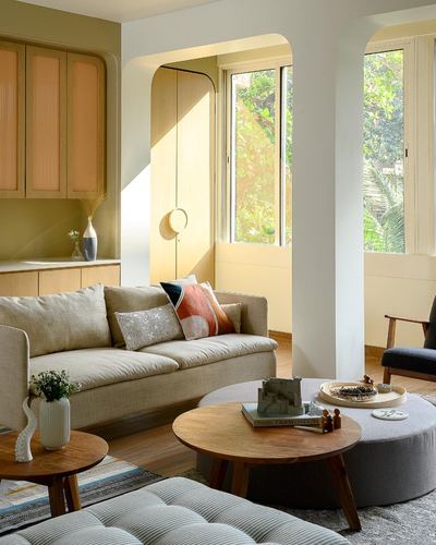 Living room with beige sofa, round wood tables, and arched yellow doorway in sunlight