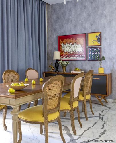 Dining room with cane chairs, mustard velvet seats, wooden table, marble floor, and framed artwork above a dark sideboard
