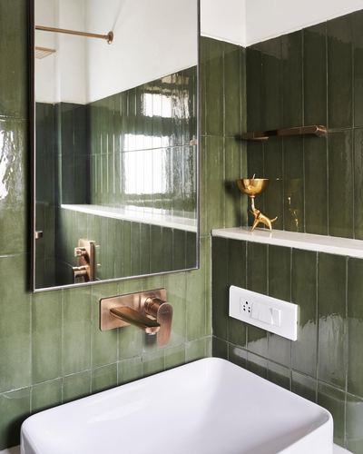 Green glossy tile bathroom with brass wall-mounted faucet and mirror above white basin