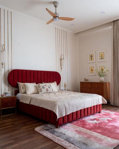 Bedroom with curved red velvet channel-tufted bed against gold-lined wall panel