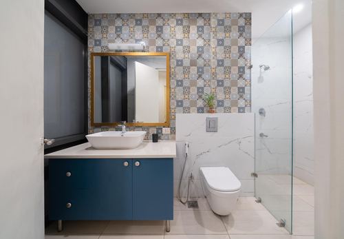 Bathroom with navy vanity, gold mirror, patchwork tile wall and marble-look shower