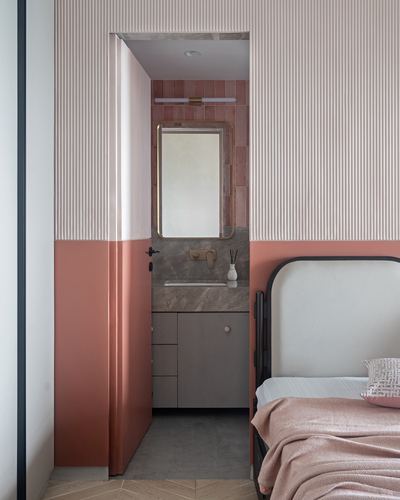 Terracotta-toned bedroom with view through open door into pink-tiled ensuite bathroom with stone vanity