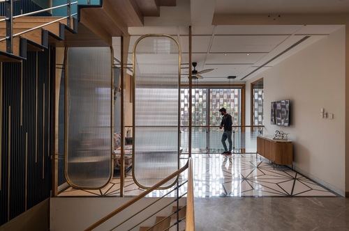 Man walking across patterned marble floor beside reeded glass brass-framed partitions in a modern Delhi home