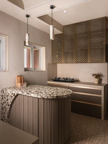 Curved terrazzo-topped kitchen island with fluted base beneath two pendant lights