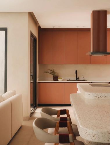 Terracotta kitchen cabinetry with ribbed hood, terrazzo island and cane-strapped stools