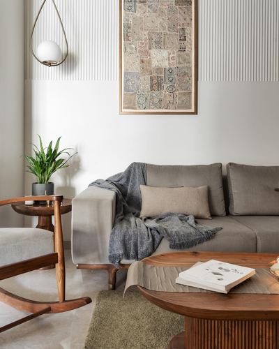 Living room with grey sofa, wooden rocking chair, round coffee table and framed textile art